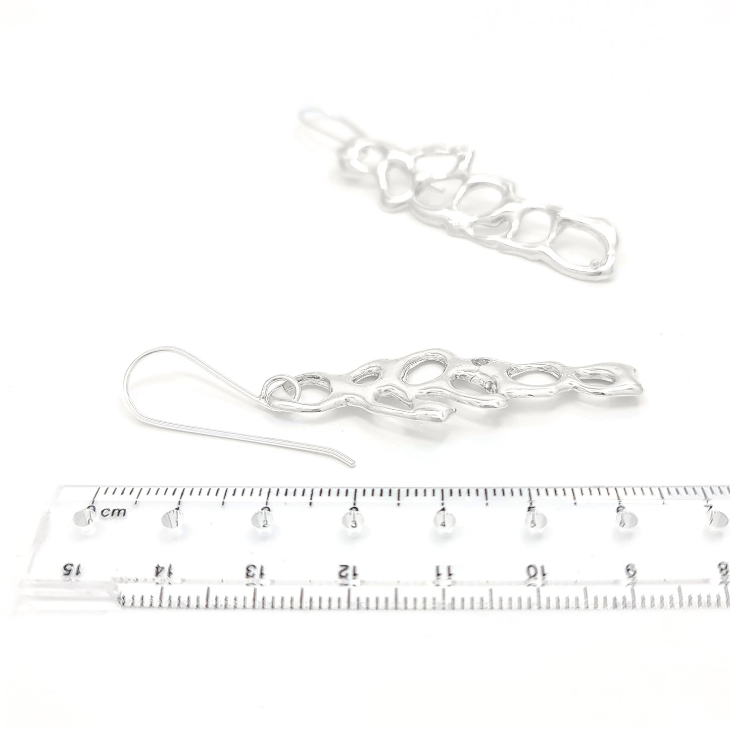 The Angel Sterling Silver Earrings from FR | Art Jewellery showcase a modern, abstract design with open, irregular oval patterns. These handmade pieces feature an elongated shape and dangle from simple hooks, boasting an exceptionally reflective polished surface.