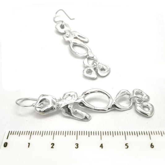 The Angel Sterling Silver Earrings from FR | Art Jewellery showcase a modern, abstract design with open, irregular oval patterns. These handmade pieces feature an elongated shape and dangle from simple hooks, boasting an exceptionally reflective polished surface.