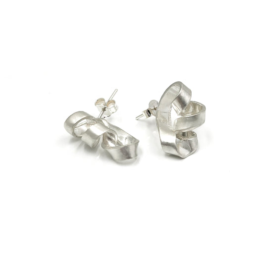 The Archi Small Sterling Silver Earrings by FR | Art Jewellery exhibit an abstract, twisted design. Every earring has a distinctive curved shape reminiscent of a fluid loop with a ribbon-like appearance, highlighting the craftsmanship of handmade jewellery.
