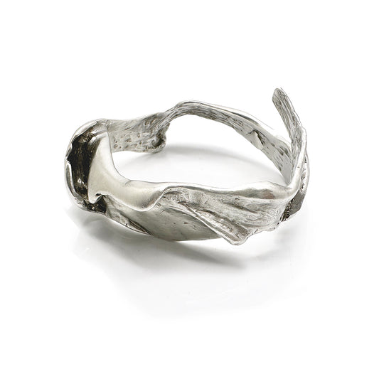 The Caracoles Sterling Silver Bangle by FR | Art Jewellery features an open-ended, sculpted design with smooth and textured surfaces, shown here resting on a white background.