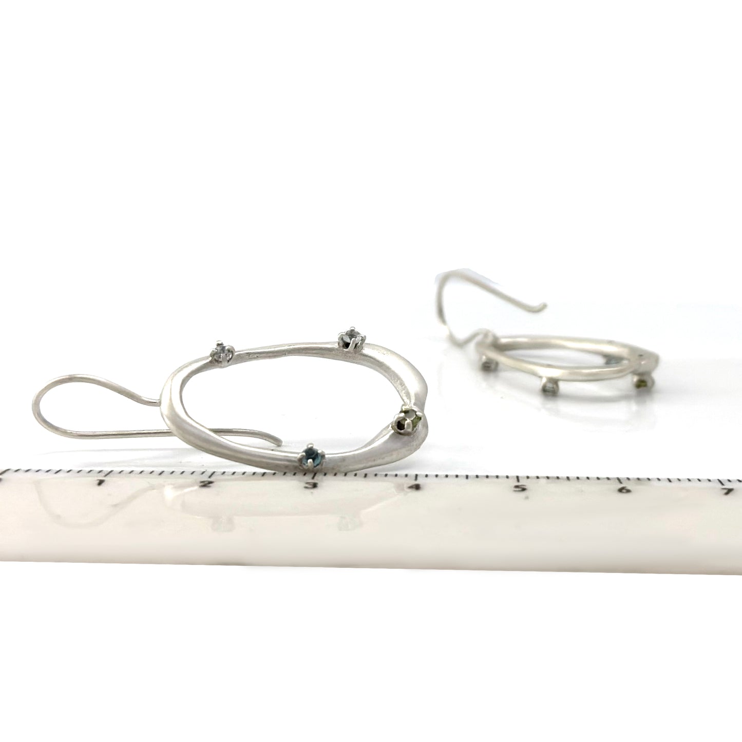 As part of the Inspired by Nature Collection from FR | Art Jewellery, the Drops Sterling Silver Earrings showcase a delicate branch-like design adorned with small blue and green gemstones. The open, asymmetrical shape adds a whimsical yet elegant touch, capturing the essence of the Blossom Series.