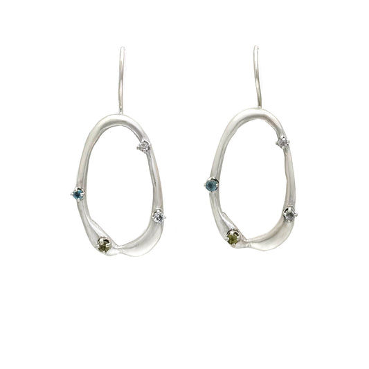 As part of the Inspired by Nature Collection from FR | Art Jewellery, the Drops Sterling Silver Earrings showcase a delicate branch-like design adorned with small blue and green gemstones. The open, asymmetrical shape adds a whimsical yet elegant touch, capturing the essence of the Blossom Series.