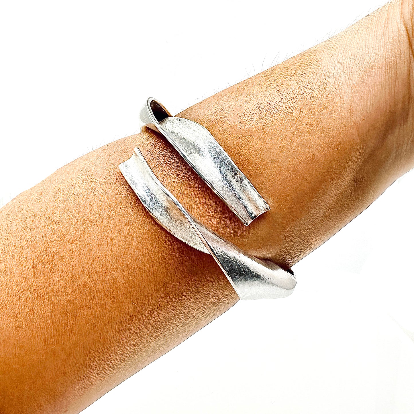 The Ebbs & Flows Bangle by FR | Art Jewellery features a twisting, asymmetrical design in polished sterling silver—a striking piece of contemporary jewellery showcased against a white background.