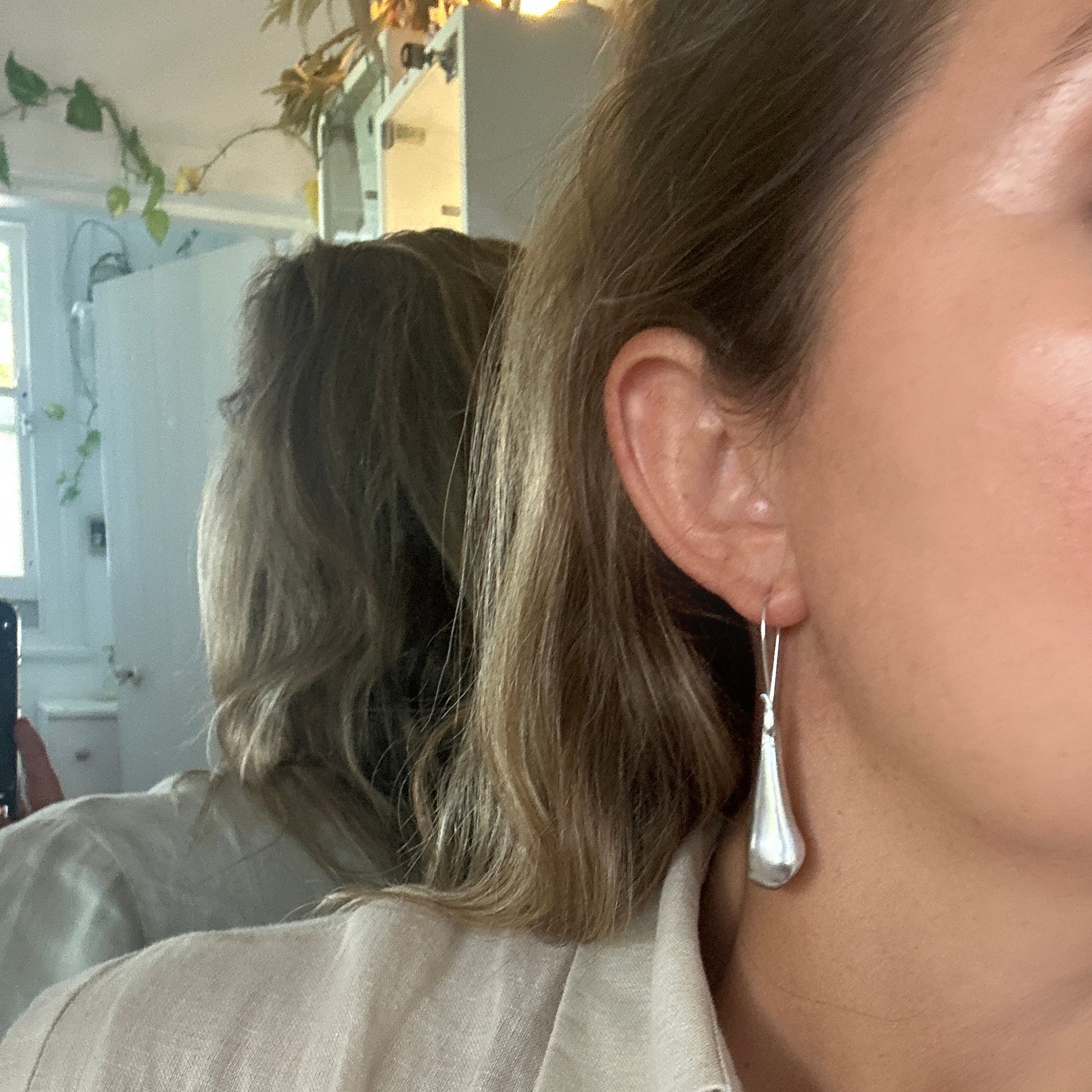 The Ebbs & Flows Earrings – Medium by FR | Art Jewellery are handcrafted sterling silver earrings featuring smooth, organic teardrop pendants and long curved hooks, shown against a white background.