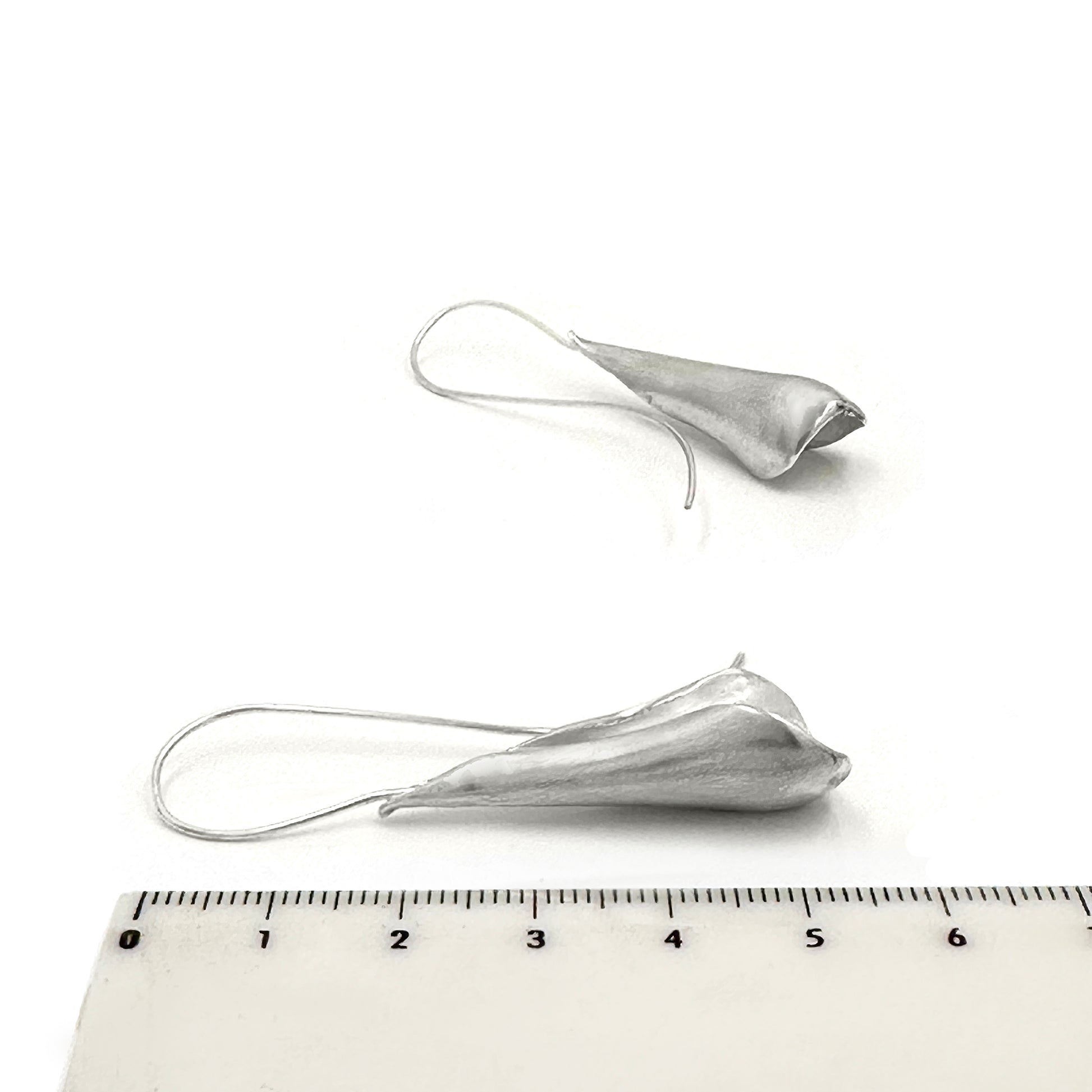 The Ebbs & Flows Earrings – Medium by FR | Art Jewellery are handcrafted sterling silver earrings featuring smooth, organic teardrop pendants and long curved hooks, shown against a white background.