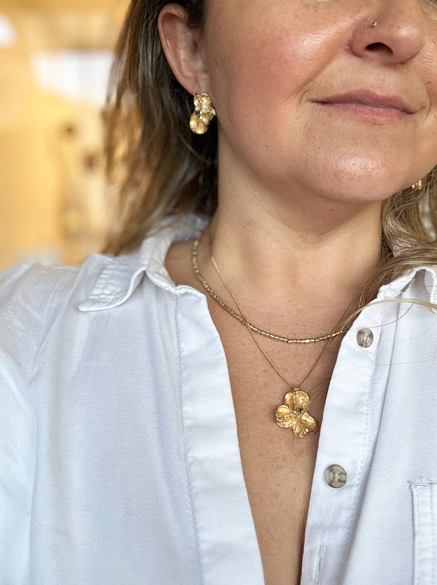 Sculptural gold-plated sterling silver pendant inspired by Australian Flindersia seed pods, set with a natural blue sapphire — handmade necklace by FR Art Jewellery. on a model