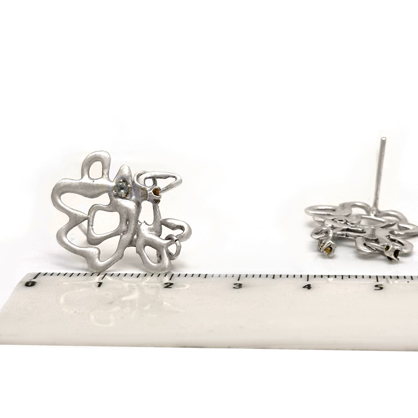 These abstract Flor sterling silver earrings from the Blossom Series by FR | Art Jewellery showcase an intricate design, with small blue stones at the center and elegantly dangling brown stones at the bottom.