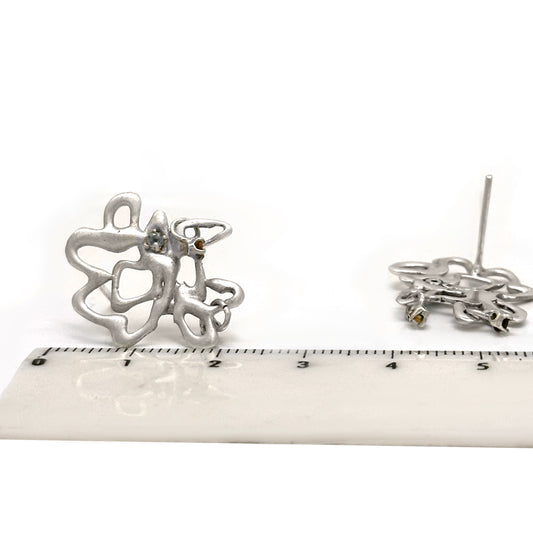 These abstract Flor sterling silver earrings from the Blossom Series by FR | Art Jewellery showcase an intricate design, with small blue stones at the center and elegantly dangling brown stones at the bottom.