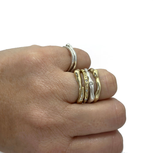 A hand displays multiple FR | Art Jewellery Freedom Diamond rings—handmade, stackable gold bands with delicate designs and small gemstones—set against a plain white background.