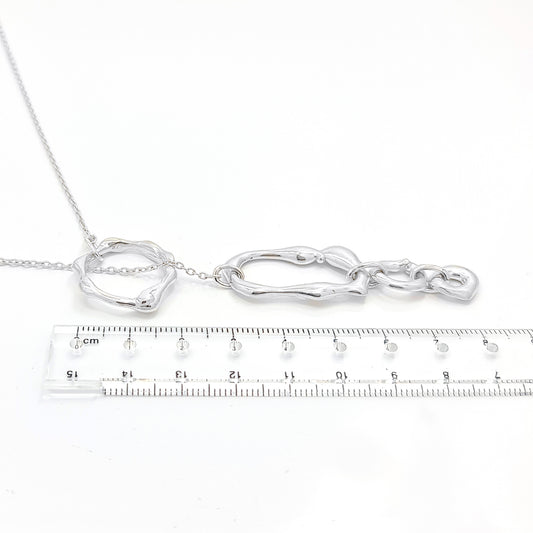 The Join Together Necklace by FR | Art Jewellery showcases a delicate design featuring a circular pendant connected by a thin chain to an asymmetrical, abstract shape. This minimalistic and elegant piece displays the abstract shape hanging below the circular pendant, creating a modern, artistic look. Each handmade piece of this jewellery can be custom-made to order.