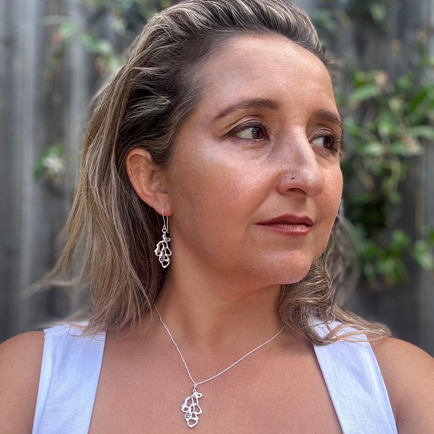 The Leaf Necklace by FR | Art Jewellery is a handmade sterling silver piece with an abstract organic pendant and a small purple gemstone, from the Blossom series, shown on a white background.