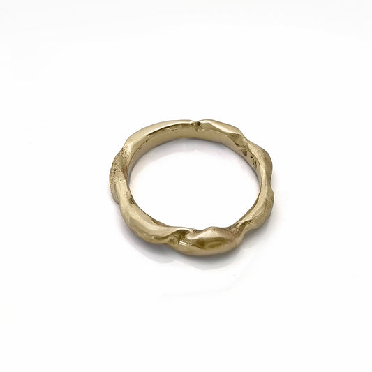 The Ocean Band by FR | Art Jewellery is a gold ring featuring a distinctive wavy texture that wraps around the band. With its polished finish and handcrafted appearance, the ring exudes an organic and artistic vibe. Subtle engravings adorn the inside of the band. This exquisite piece of handmade jewellery is showcased against a white background.