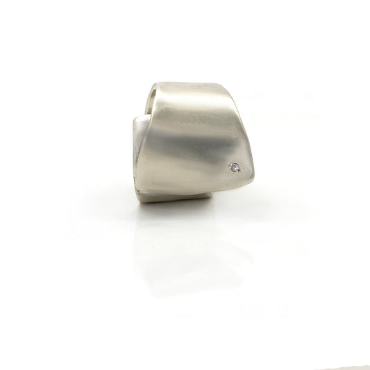 The Spiral Flow Ring by FR | Art Jewellery is a modern sterling silver ring featuring a smooth, sculptural form and a small inset diamond, shown on a white reflective surface.