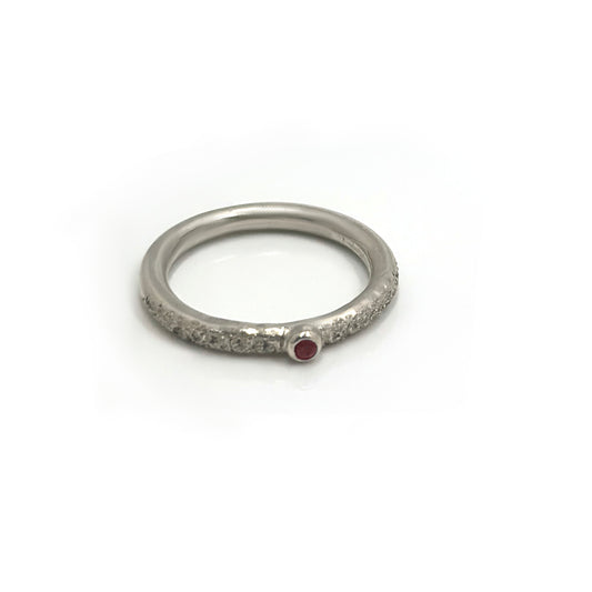 The FR | Art Jewellery Tinytoo Sterling Silver Ring with Ruby Gemstone features a textured band and a small round ruby, elegantly displayed on a white background.