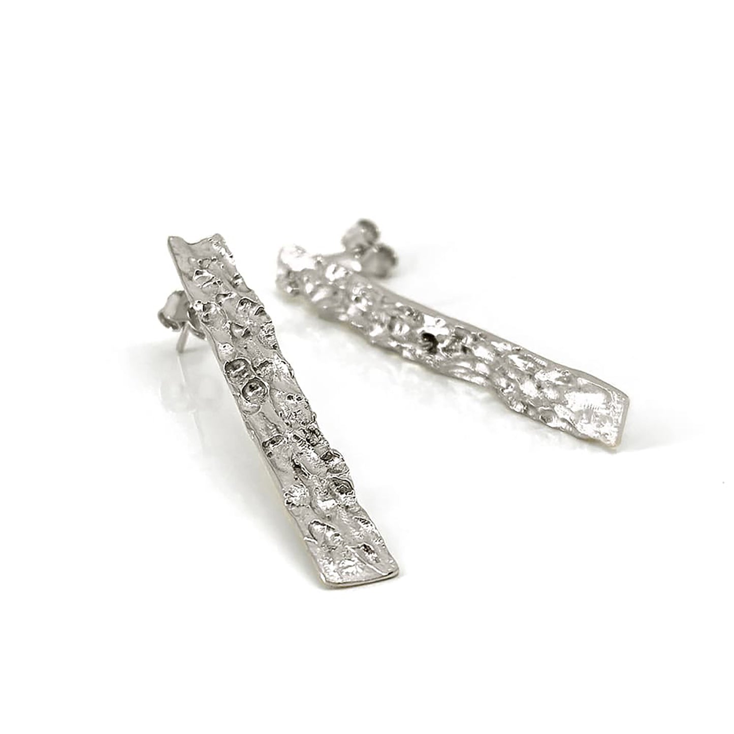 The Tribu Long Earrings in Sterling Silver by FR | Art Jewellery feature an irregular, organic shape and post backing, making a bold statement for your handmade jewellery collection. Shown lying on a white surface.