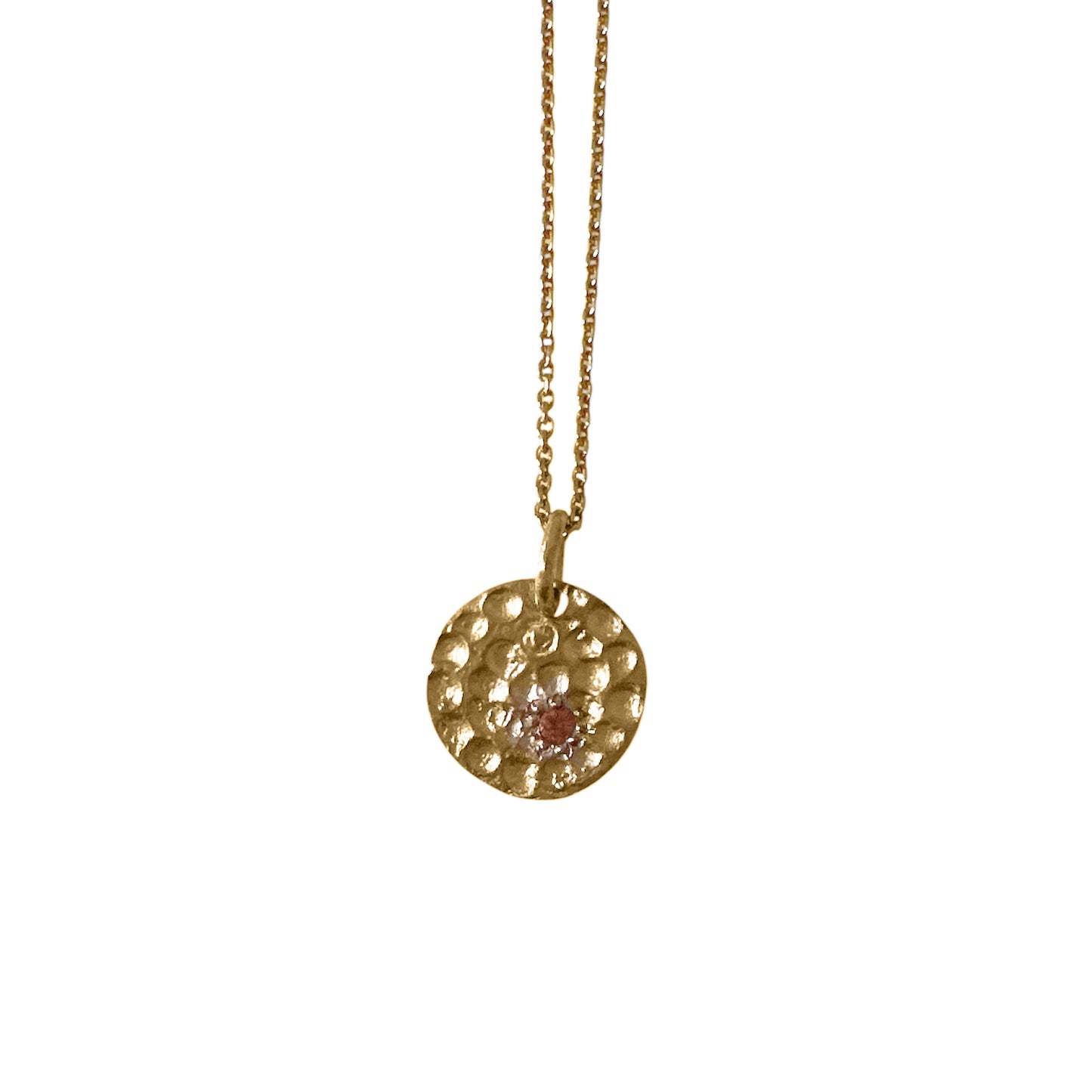 The Spot of Light necklace by FR | Art Jewellery is a gold-plated piece with a textured round pendant featuring a central garnet gemstone, beautifully showcased against a white background.