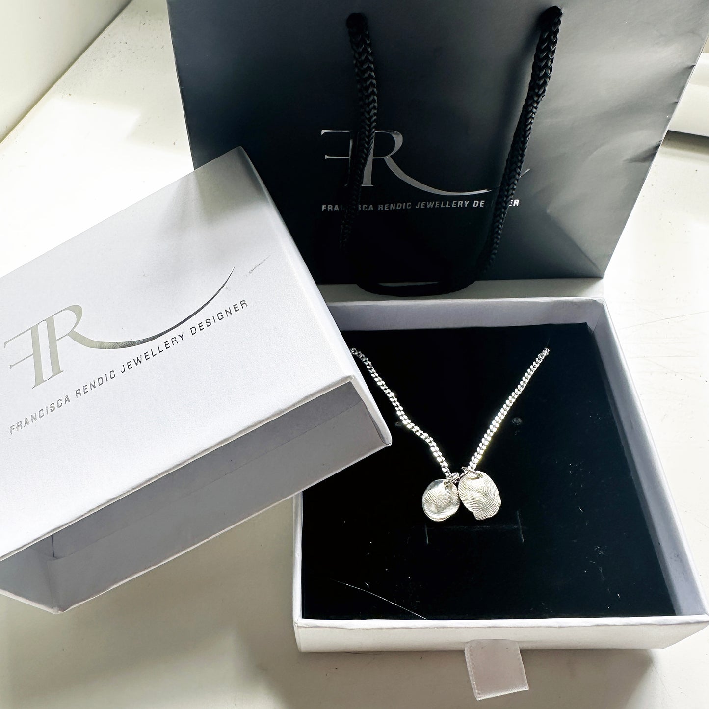 Introducing the Fingerprint Sterling Silver Necklace by FR | Art Jewellery, featuring two round pendants with custom impressions, elegantly hanging from a delicate chain against a white background.