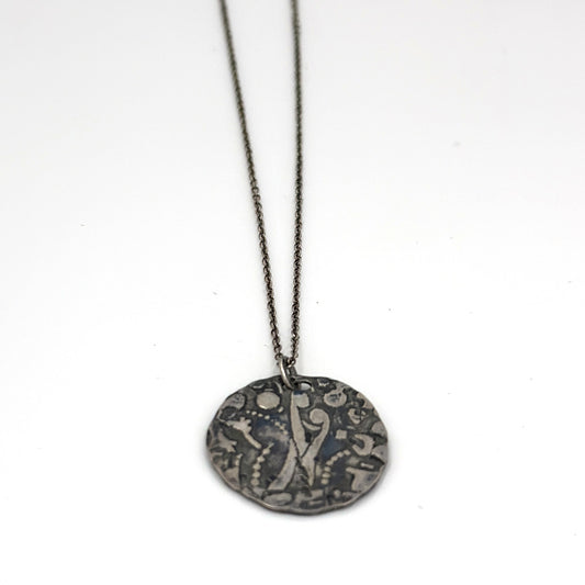 The Symbol Hug Necklace Sterling Silver by FR | Art Jewellery features a delicate chain and a coin-shaped, etched pendant with a dark, textured finish, embodying love and intrigue against a plain white background.