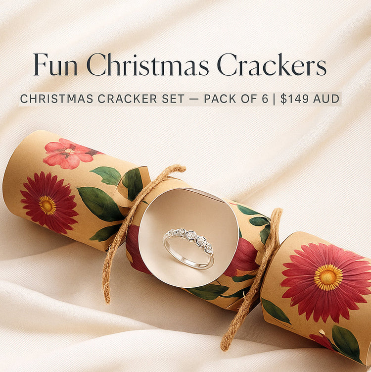 A floral Christmas cracker set with a ring inside is displayed on a soft cream fabric. Text reads: "Fun Christmas Crackers, pack of 6, $149 AUD.