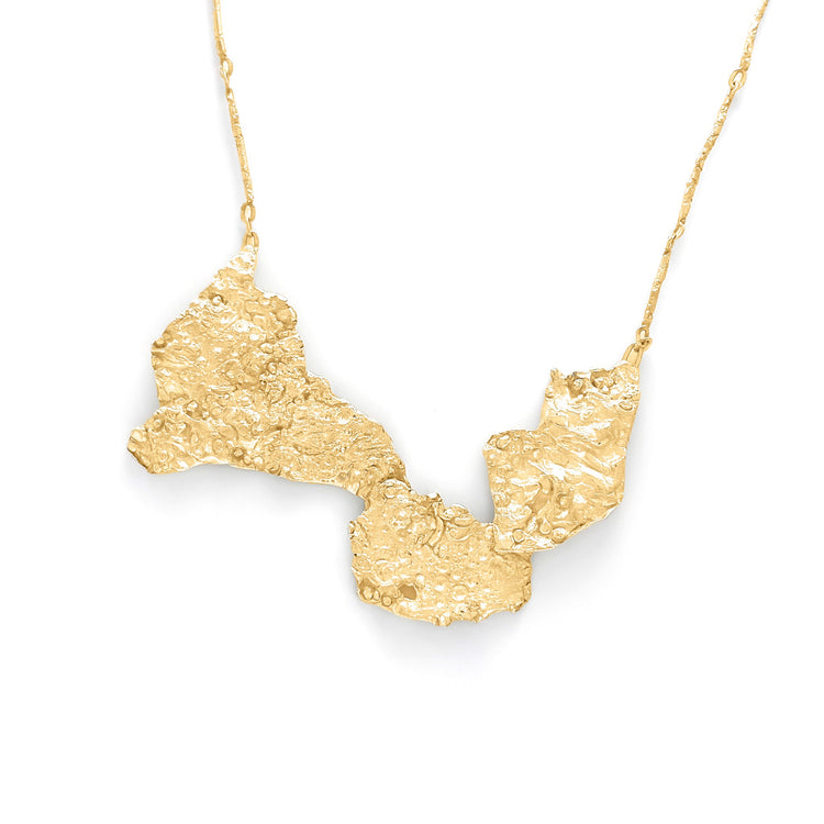 A gold necklace with a textured, abstract pendant featuring irregular shapes and a hammered finish, suspended on a delicate chain.