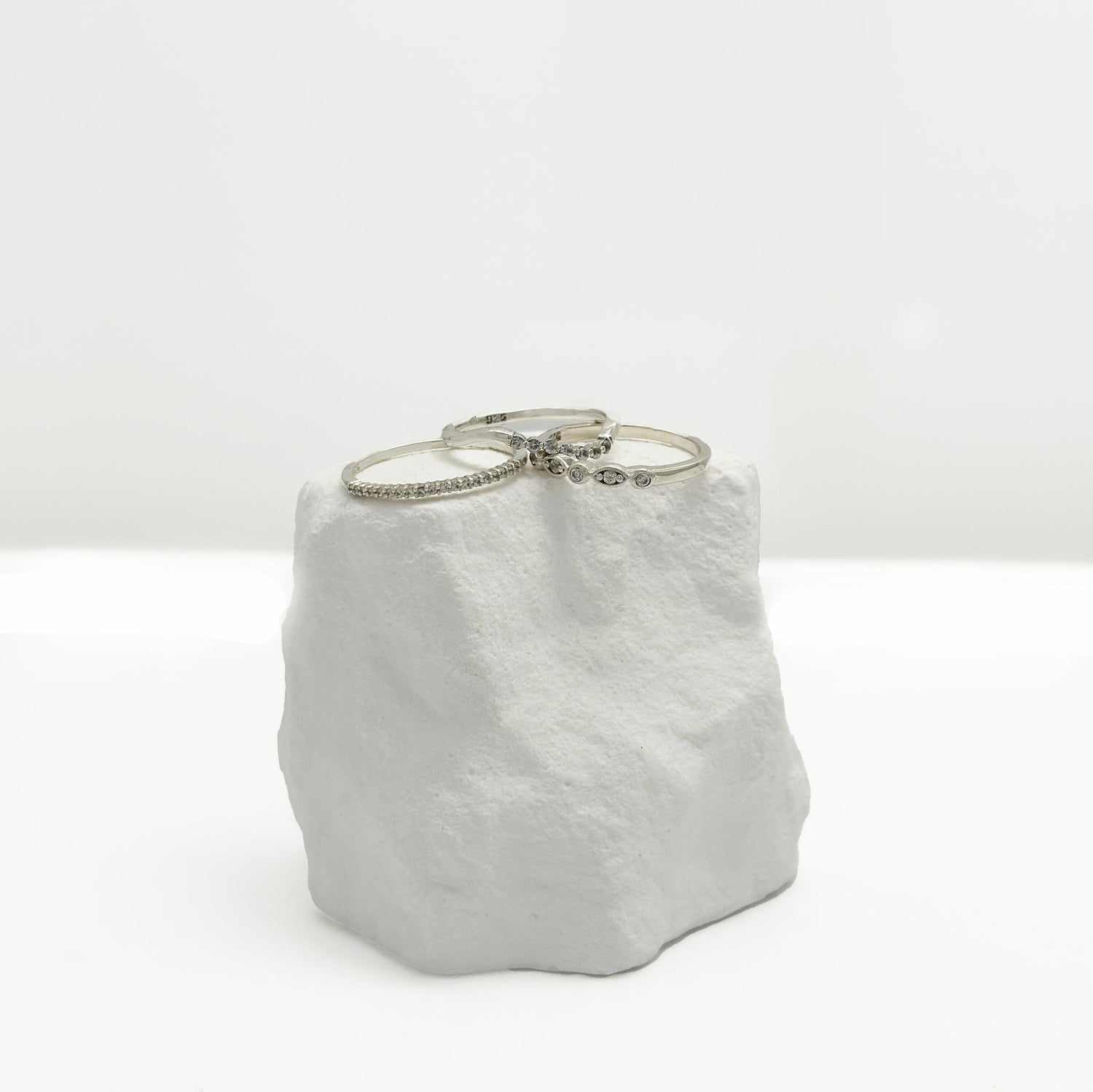 Two silver bracelets, one with small stones and the other with a delicate leaf design, displayed on a textured white stone against a plain white background.