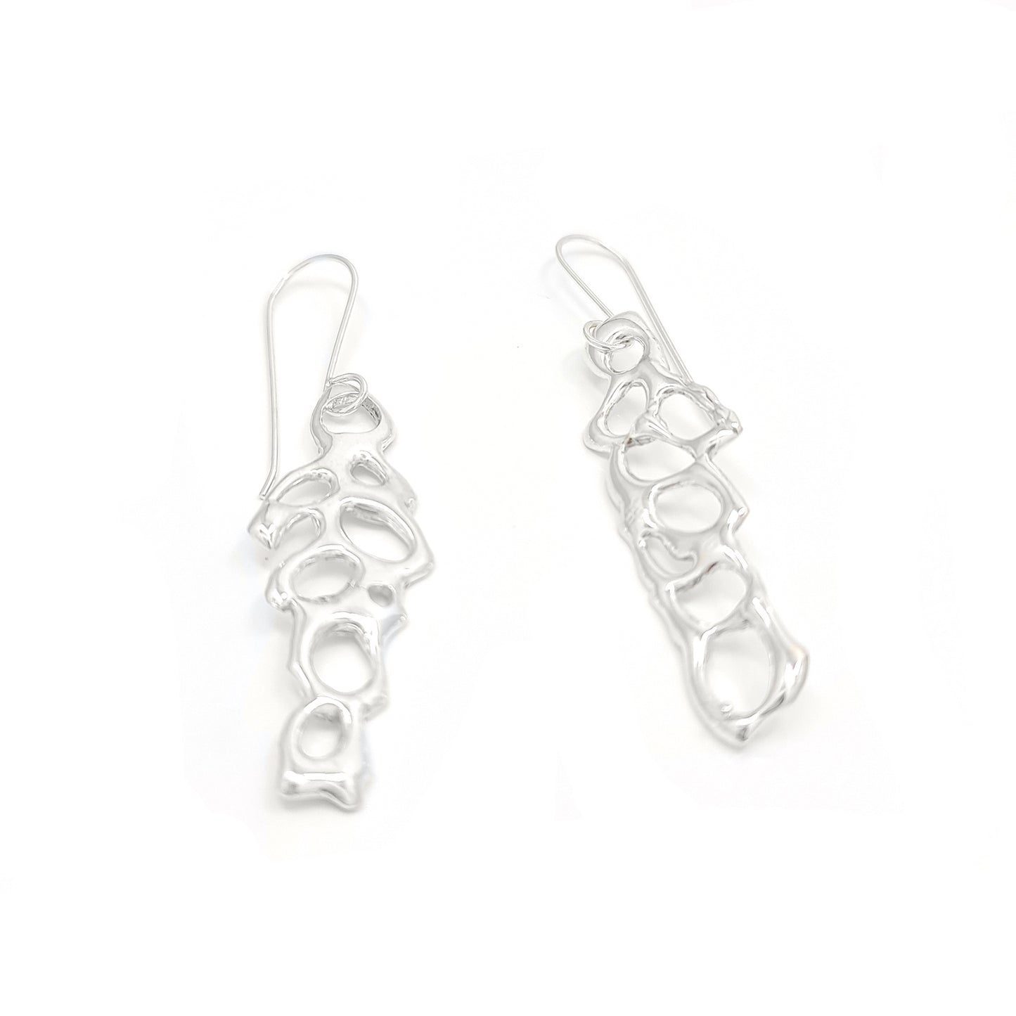 Introducing the "Angel Earrings" by FR | Art Jewellery: a stunning pair of silver earrings featuring an abstract, organic design with irregularly shaped open cutouts. This handmade jewellery piece boasts long hooks for easy insertion into pierced ears and a shiny, polished finish.