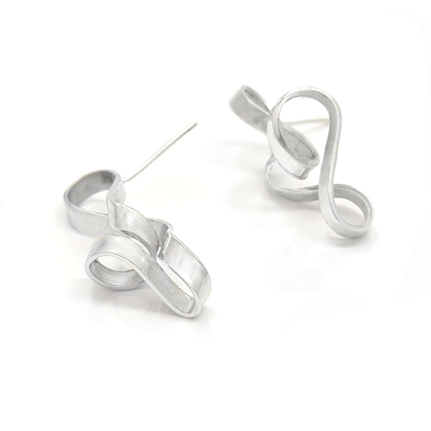 The Archi Small Earrings by FR | Art Jewellery feature two silver-colored, abstract metal pieces shaped like elegant, flowing ribbons. Each earring twists and curves, creating unique and artistic forms. The surface is smooth with a slightly reflective finish that accentuates the curves, exemplifying the beauty of handmade jewellery.