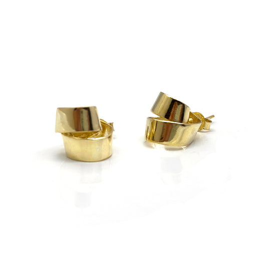 A pair of FR | Art Jewellery's Mini Archi Studs, featuring a handmade, gold-plated, slightly curved ribbon-like design set against a white background. The studs boast a glossy finish that beautifully reflects light.