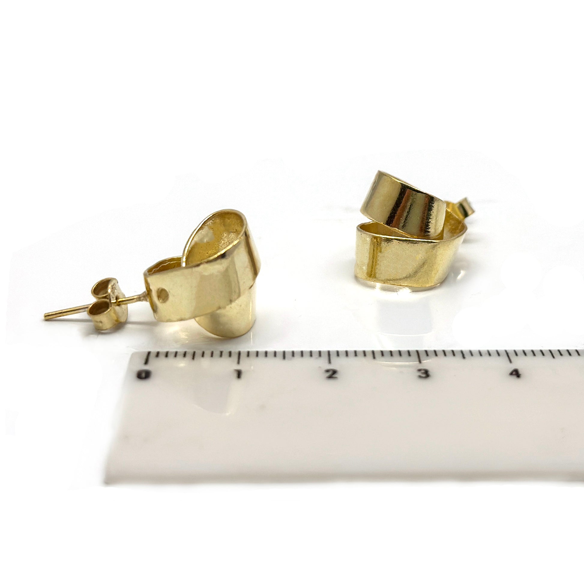 A pair of FR | Art Jewellery's Mini Archi Studs, featuring a handmade, gold-plated, slightly curved ribbon-like design set against a white background. The studs boast a glossy finish that beautifully reflects light.