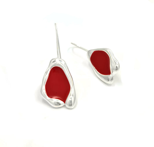 A pair of teardrop-shaped earrings with a shiny red center, laid on a white surface. The Colour Bubble Earrings by FR | Art Jewellery feature a modern, abstract design with smooth, fluid lines and a glossy finish, crafted from gold-plated 925 sterling silver.