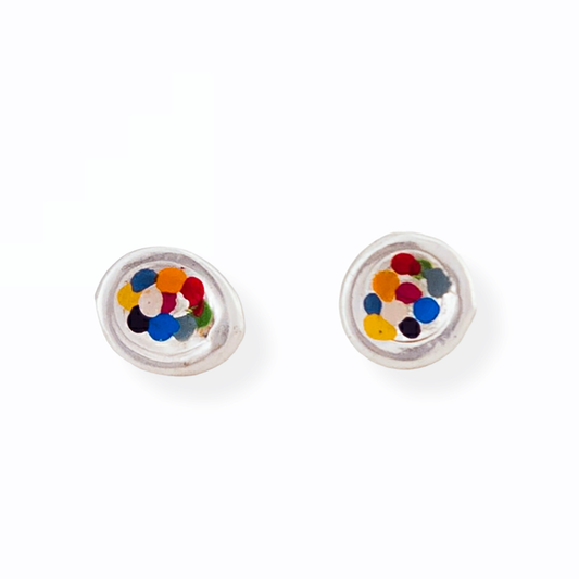 The Colour Dot Earrings Rainbow by FR | Art Jewellery are a pair of silver stud earrings featuring multi-colored confetti-like pieces embedded inside transparent domes. The randomly arranged confetti includes colors such as blue, yellow, orange, and red, all within a simple, circular design.