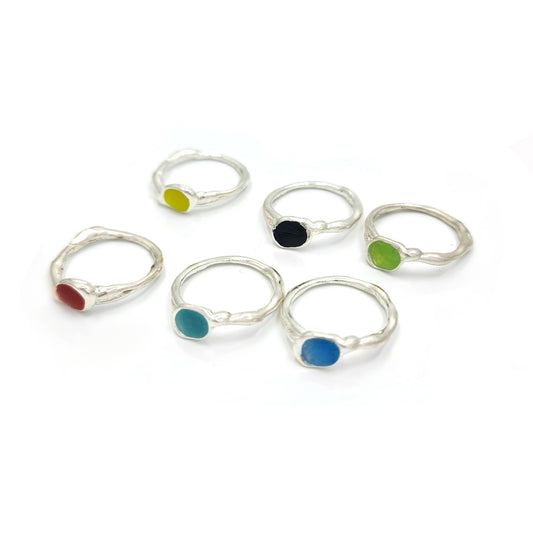 Explore the Colour Dot rings from FR | Art Jewellery, showcasing a collection of six sterling silver rings adorned with vibrant circular stones in red, yellow, black, green, turquoise, and blue. Displayed elegantly in two rows on a white background, each ring adds a bold splash of color to complement your ensemble.