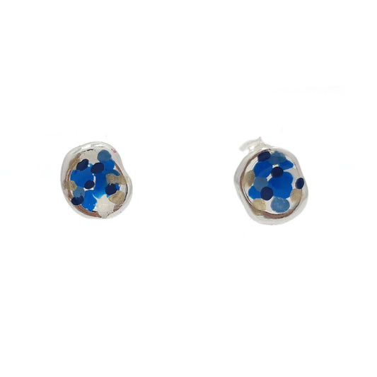 A pair of Colour Dot Earrings Sky by FR | Art Jewellery features a round silver base adorned with a mosaic design of small, scattered blue and black dots against a light neutral background. They are presented side by side on a plain white surface.