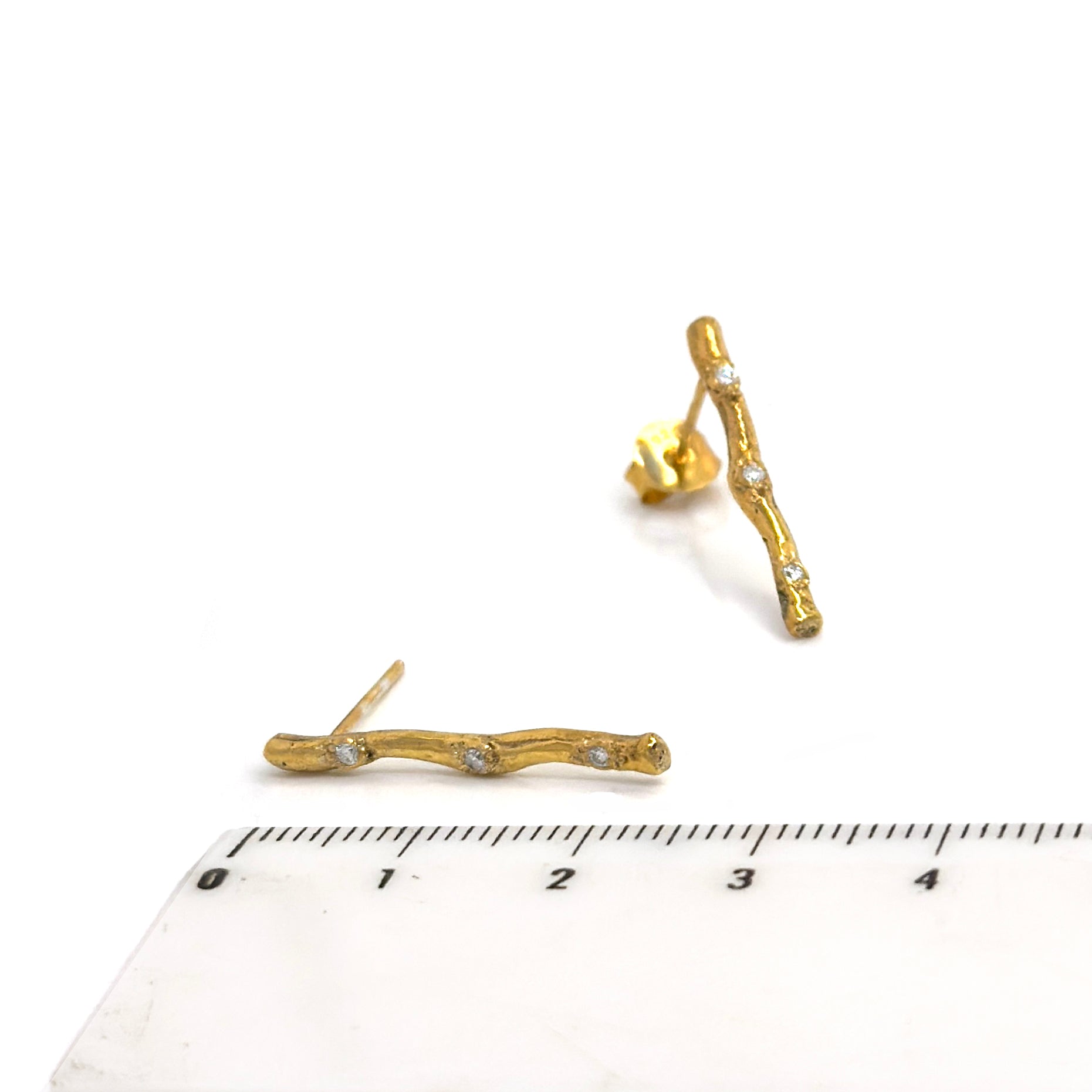 FR | Art Jewellery's Diamond Twig Earrings – Gold Plated in Sterling Silver feature a textured, nature-inspired design with clear gemstones; one earring stands upright, the other lies flat to showcase its elegant post.