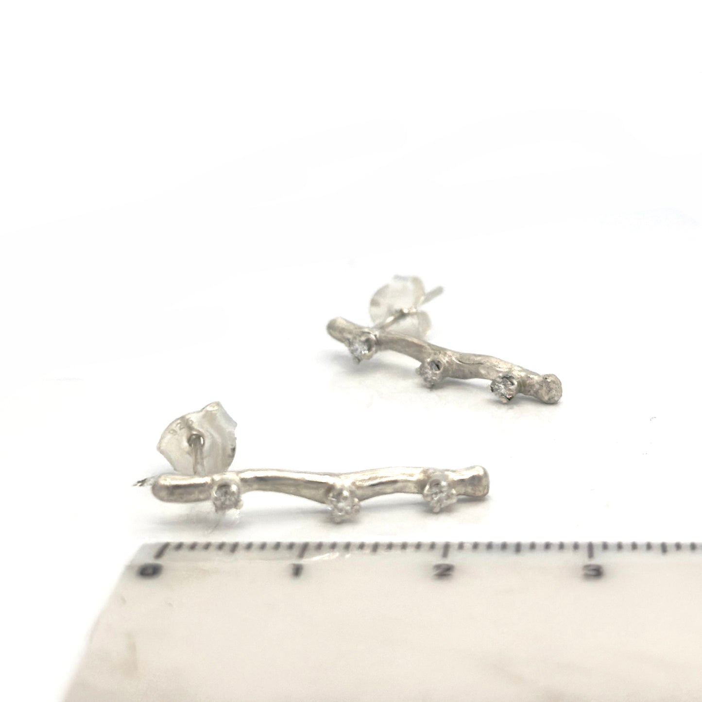Silver branch-shaped earrings on a white background with a ruler for scale.