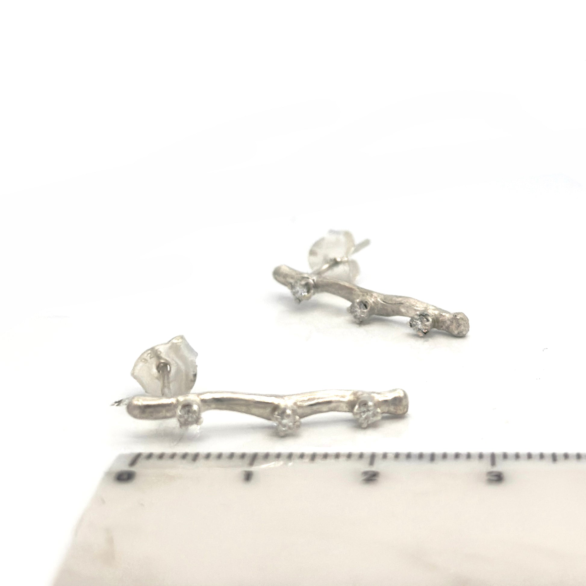 Silver branch-shaped earrings on a white background with a ruler for scale.
