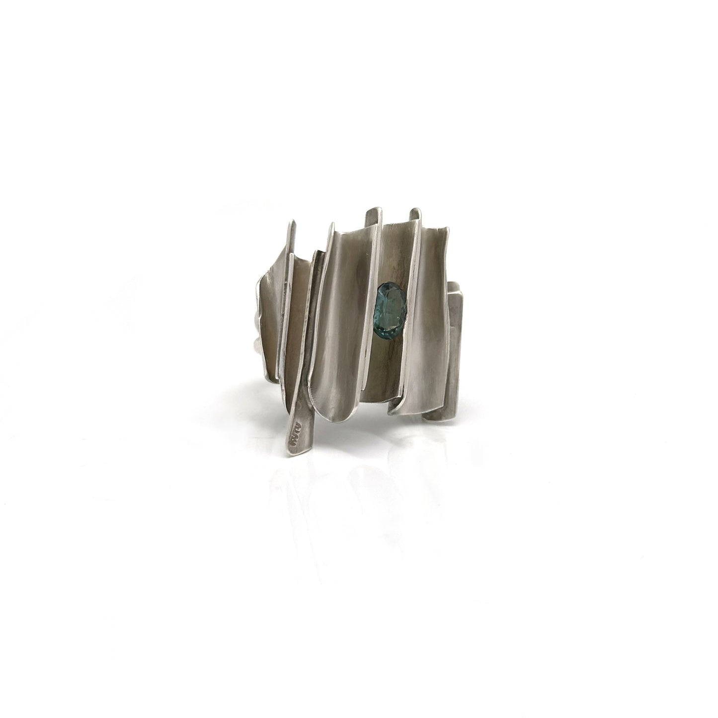 Pictured is the Encrusted Ring by FR | Art Jewellery, a striking piece of handmade jewelry featuring a unique wavy and layered design. This wide, silver ring boasts an elongated, oval-shaped green gemstone set asymmetrically within one of the wavy layers, creating an abstract and modern aesthetic. The ring stands out beautifully against the white background.