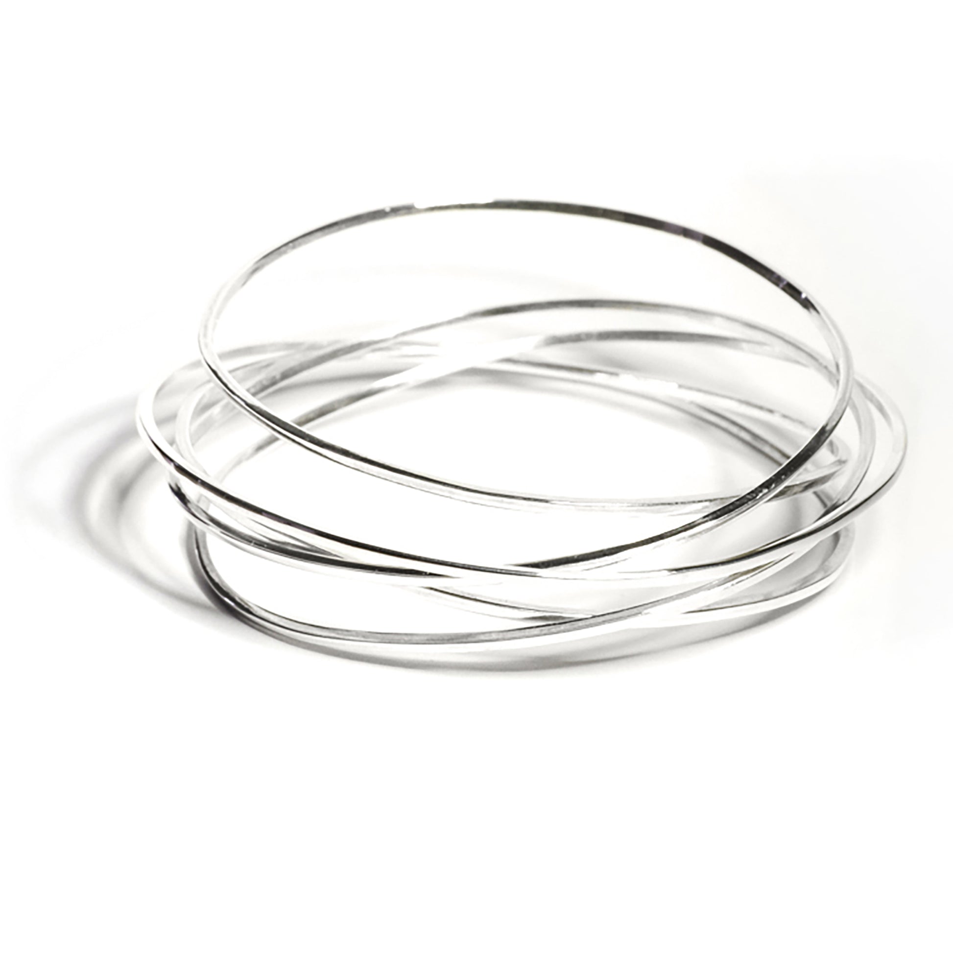 A set of thin, silver Endless Bangles from FR | Art Jewellery slightly overlap each other on a white surface. These simple yet elegant bangles feature a smooth, reflective finish and are part of our exclusive handmade jewellery collection. Custom-made orders and gold plating options are also available for these sophisticated pieces.