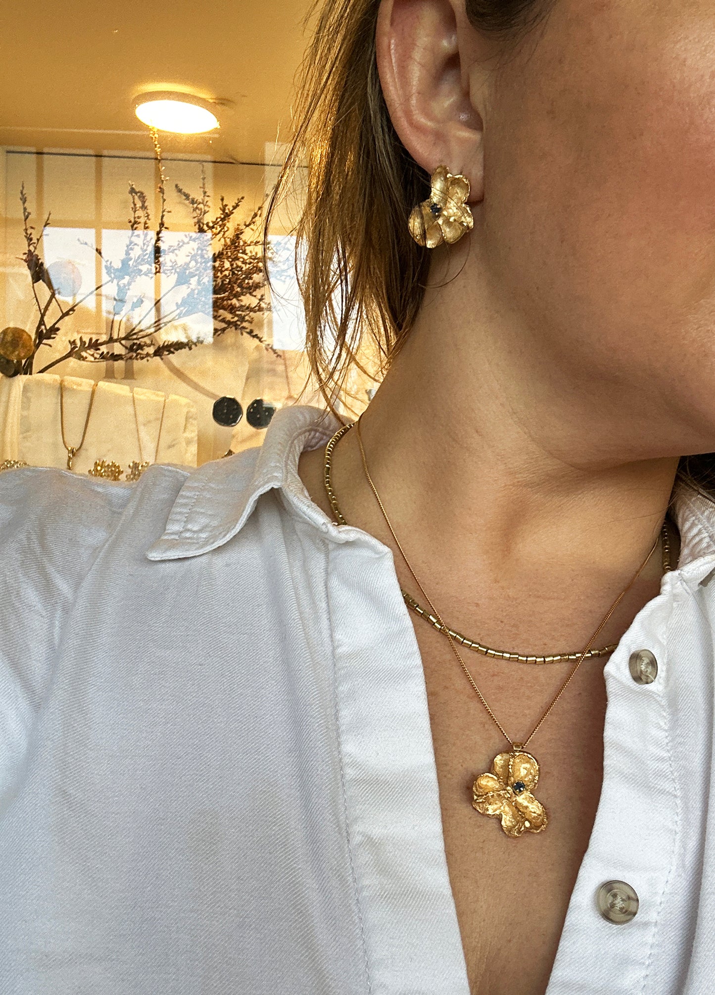 Gold-plated sterling silver sculptural stud earrings inspired by Flindersia seed pods with blue sapphires set in the centre — handmade by FR Art Jewellery. on model