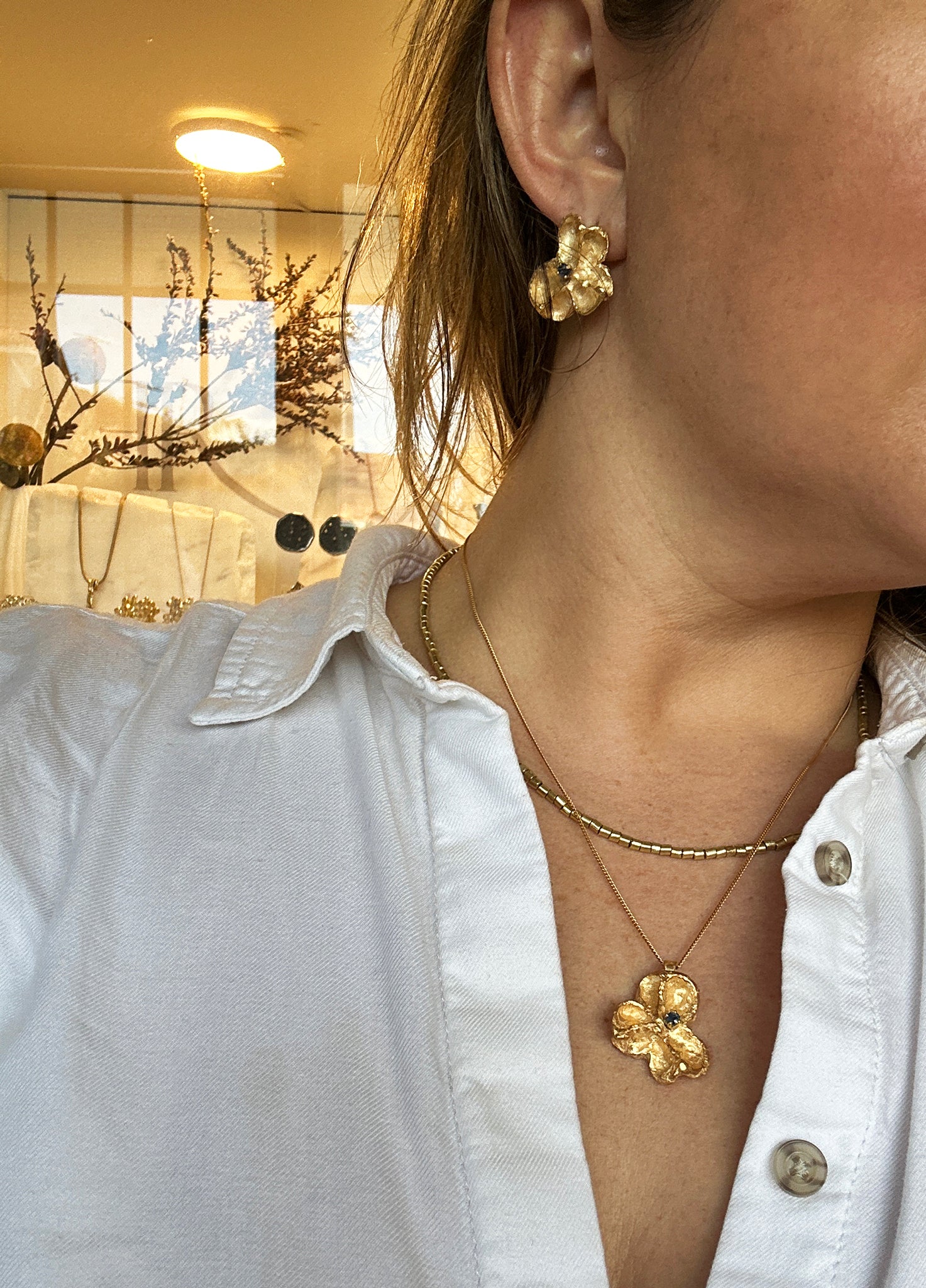 Gold-plated sterling silver sculptural stud earrings inspired by Flindersia seed pods with blue sapphires set in the centre — handmade by FR Art Jewellery. on model