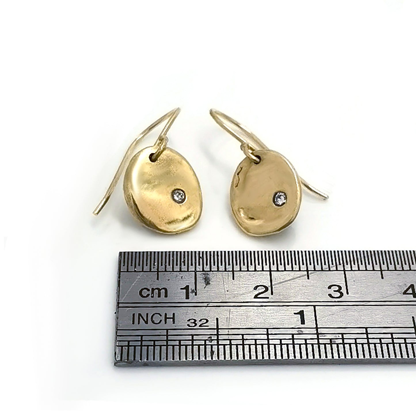 A pair of elegant Full Moon Earrings by FR | Art Jewellery, each featuring a small, round diamond set in the center. The gold discs have a slightly irregular, organic shape, giving them a unique and artisanal appearance. These handmade jewellery pieces are attached to slim hooks for wearing.