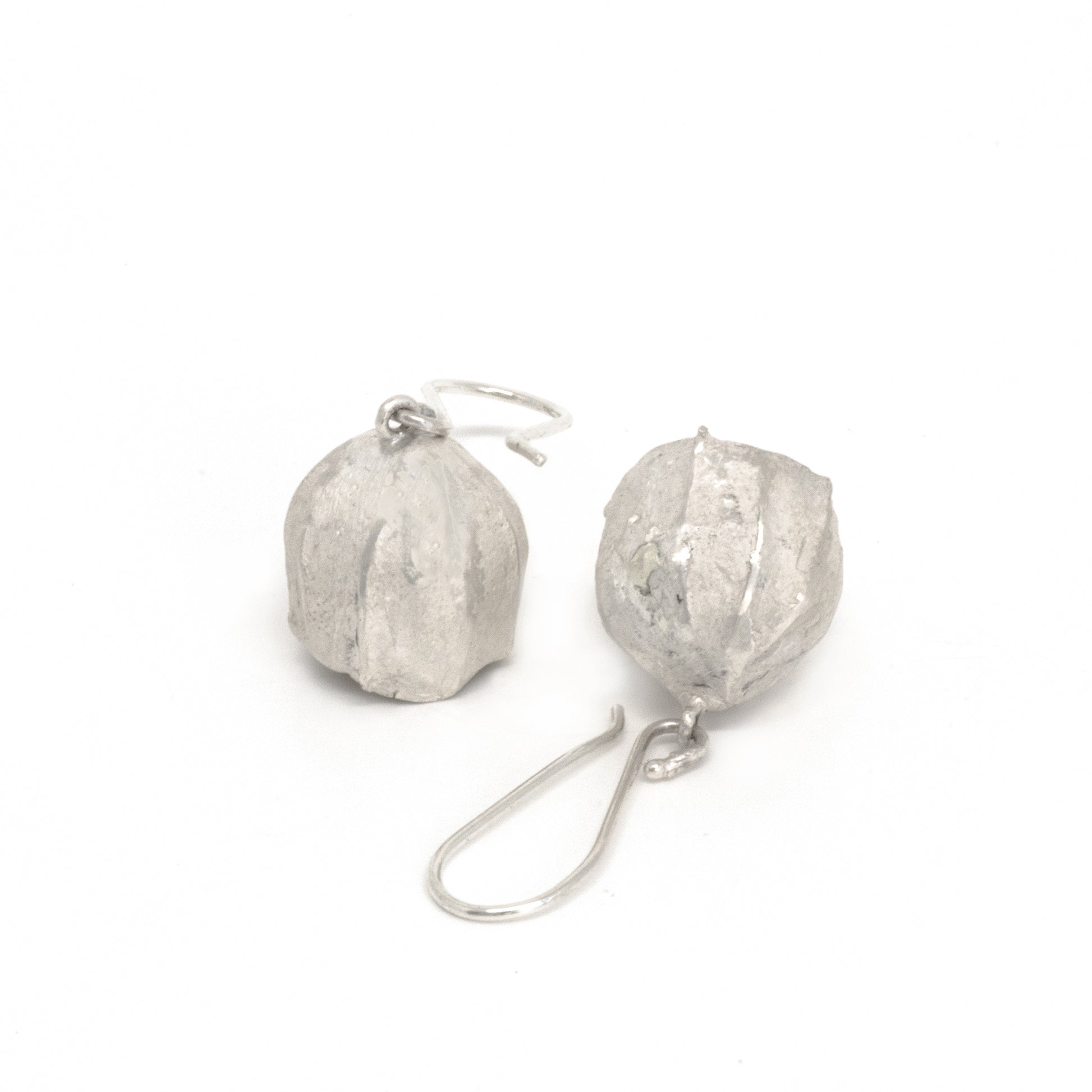 Close-up of a pair of FR | Art Jewellery's Gum Seeds Earrings. Each earring showcases a silver, rounded, slightly crumpled textured bulb dangling from a delicate hook. The earrings are laid out on a white background with the hooks intersecting. These elegant pieces are part of our handmade jewellery collection, perfect for custom-made orders.