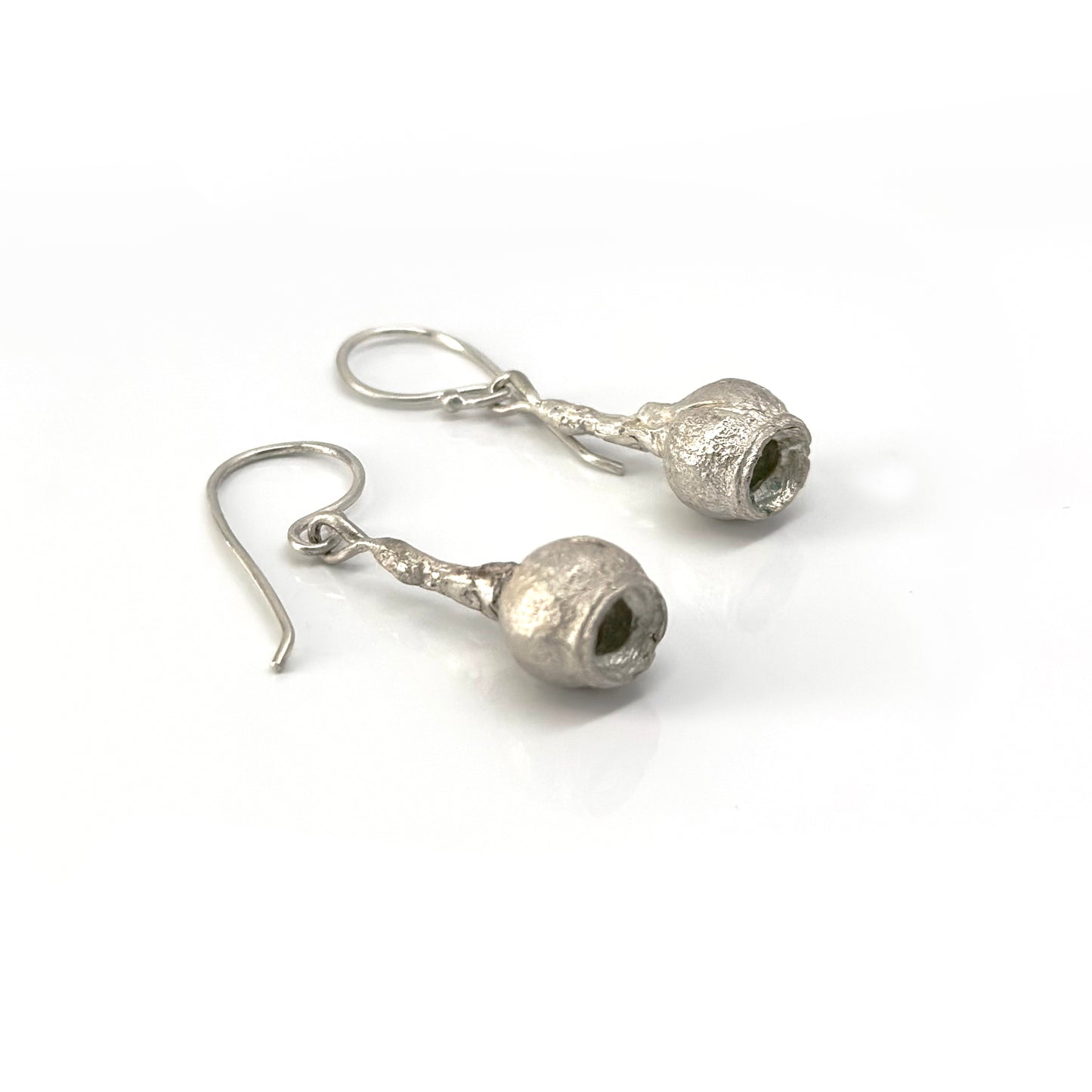 Introducing the Gummies Earrings by FR | Art Jewellery: a pair of silver drop earrings, each showcasing a textured spherical charm with a hollow center. These earrings, meticulously crafted from sterling silver and enhanced with subtle gold plating, hang gracefully from simple hooks and exude a slightly rustic, handcrafted appearance.