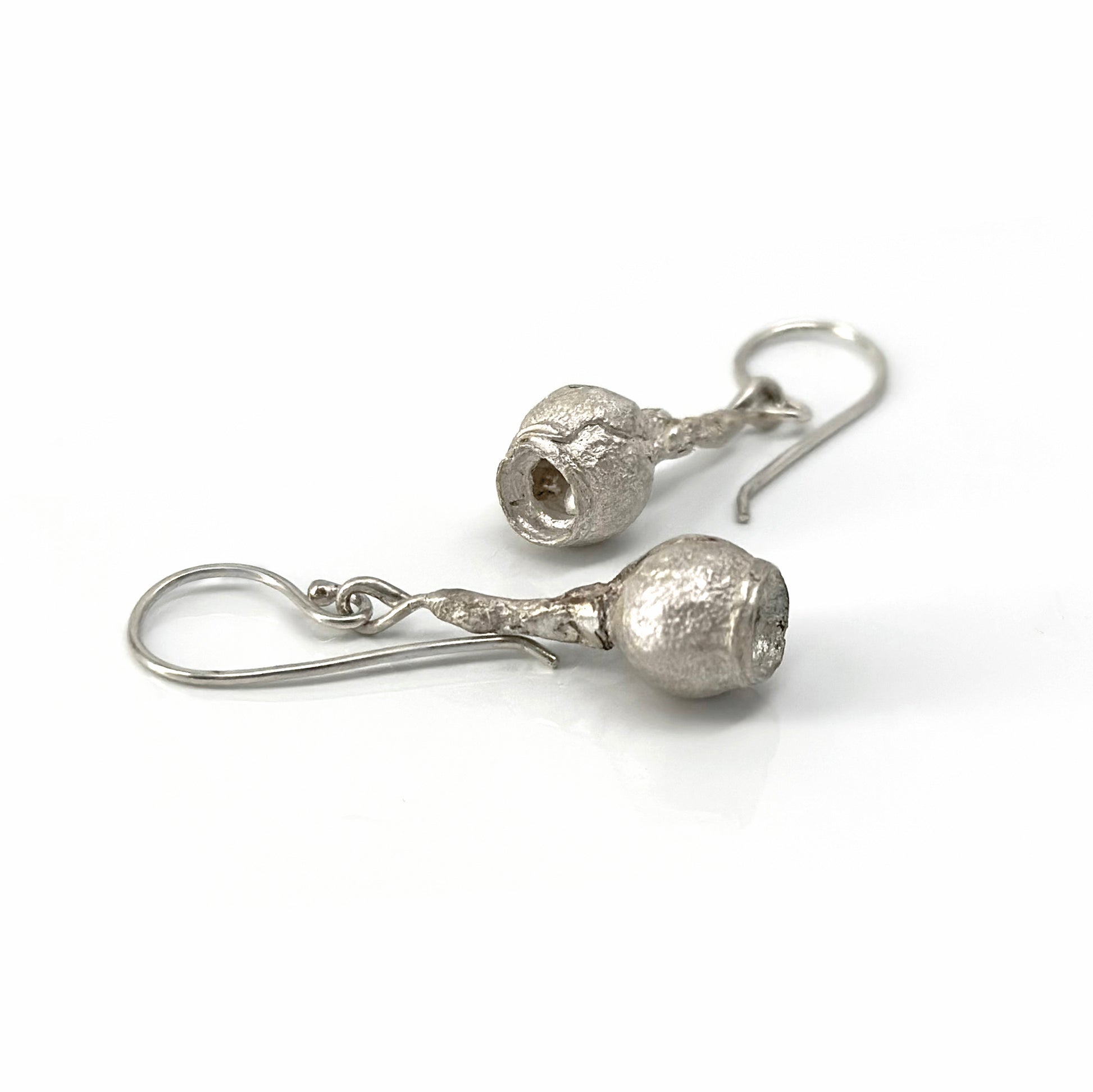 Introducing the Gummies Earrings by FR | Art Jewellery: a pair of silver drop earrings, each showcasing a textured spherical charm with a hollow center. These earrings, meticulously crafted from sterling silver and enhanced with subtle gold plating, hang gracefully from simple hooks and exude a slightly rustic, handcrafted appearance.