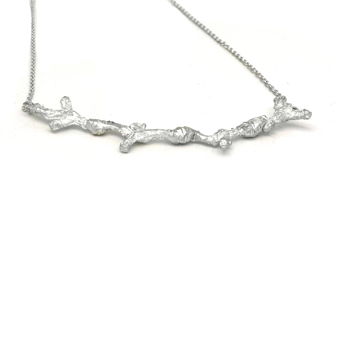 The Branches Necklace from FR | Art Jewellery features a delicate silver chain and a pendant shaped like a textured, intricate tree branch, capturing the essence of handmade jewellery and natural design.