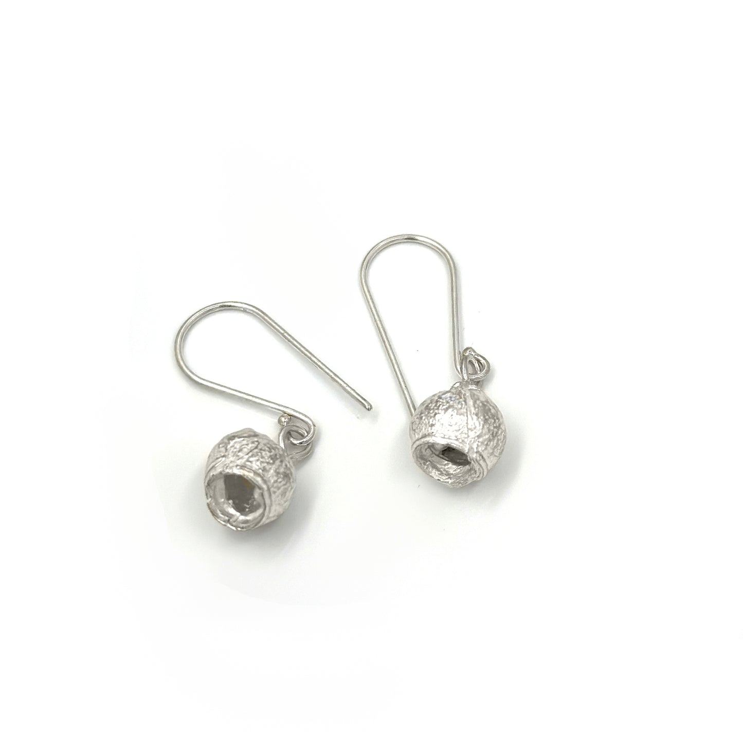 The "Gummy Earrings" by FR | Art Jewellery are a stunning pair of silver drop earrings featuring a textured hollow spherical design. The spheres are attached to hooks, allowing them to dangle freely. Simple and elegant with a minimalist yet stylish look, these handmade pieces showcase exceptional craftsmanship. Photographed against a white background, they make an exquisite addition to any jewellery collection.