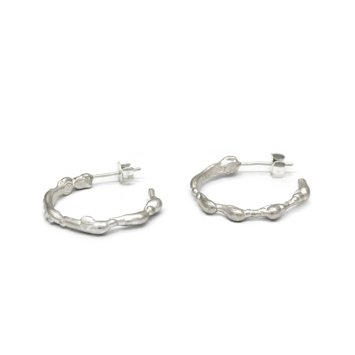 A pair of small, irregularly shaped Hoop 25mm earrings made of sterling silver with a textured, organic design by FR | Art Jewellery. Each earring features a post and butterfly clasp closure and is part of the Curves Collection, displayed against a plain white background.