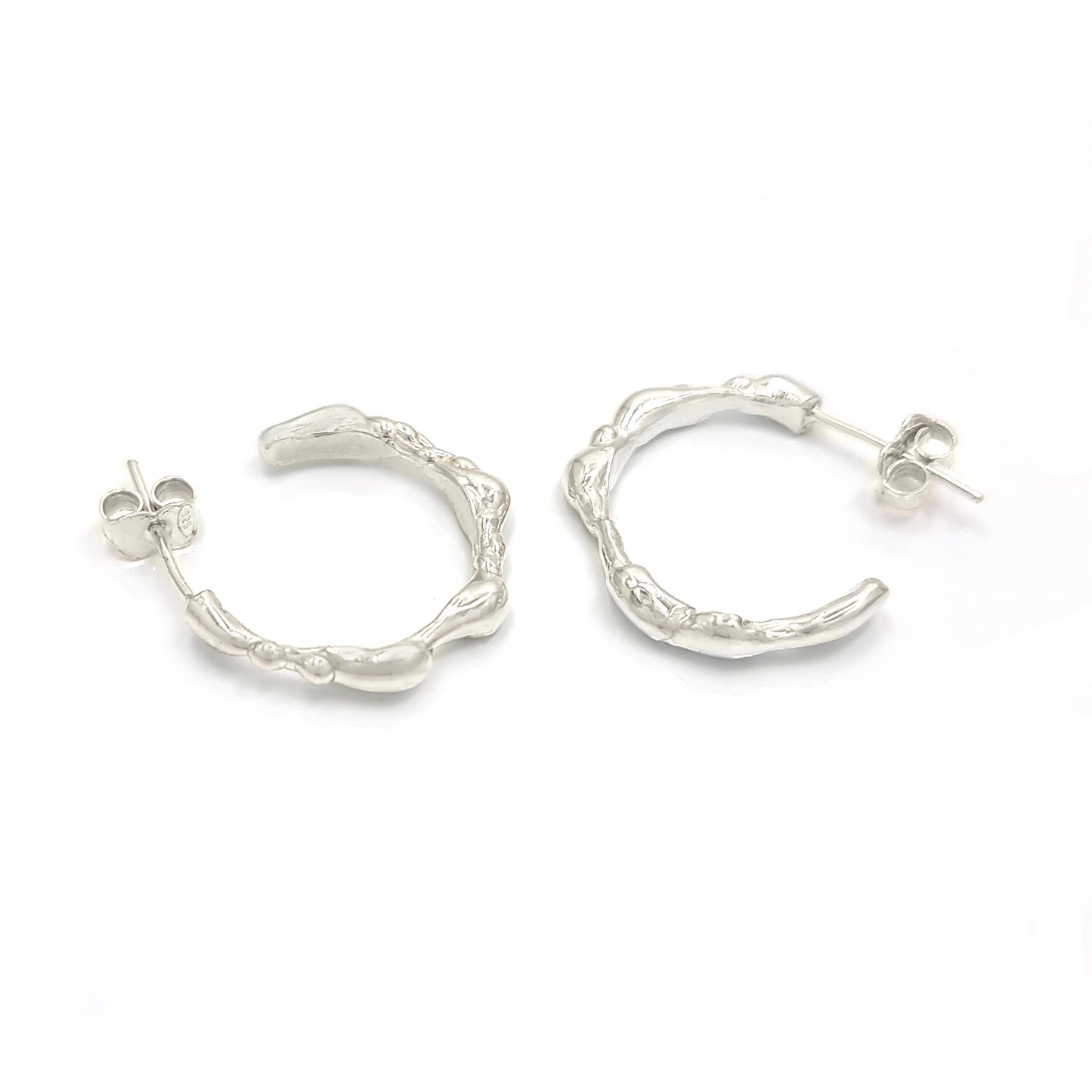 A pair of small, irregularly shaped Hoop 25mm earrings made of sterling silver with a textured, organic design by FR | Art Jewellery. Each earring features a post and butterfly clasp closure and is part of the Curves Collection, displayed against a plain white background.