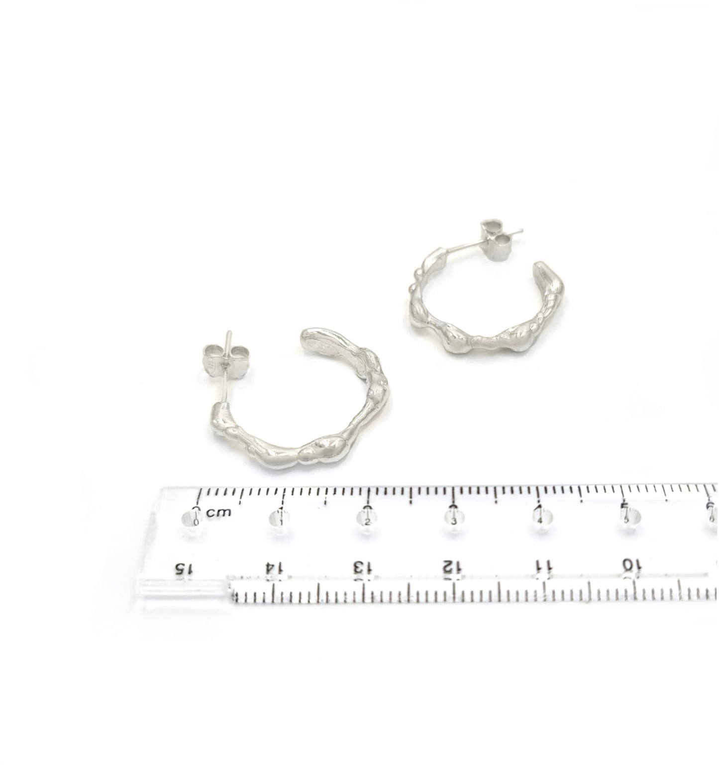 A pair of small, irregularly shaped Hoop 25mm earrings made of sterling silver with a textured, organic design by FR | Art Jewellery. Each earring features a post and butterfly clasp closure and is part of the Curves Collection, displayed against a plain white background.