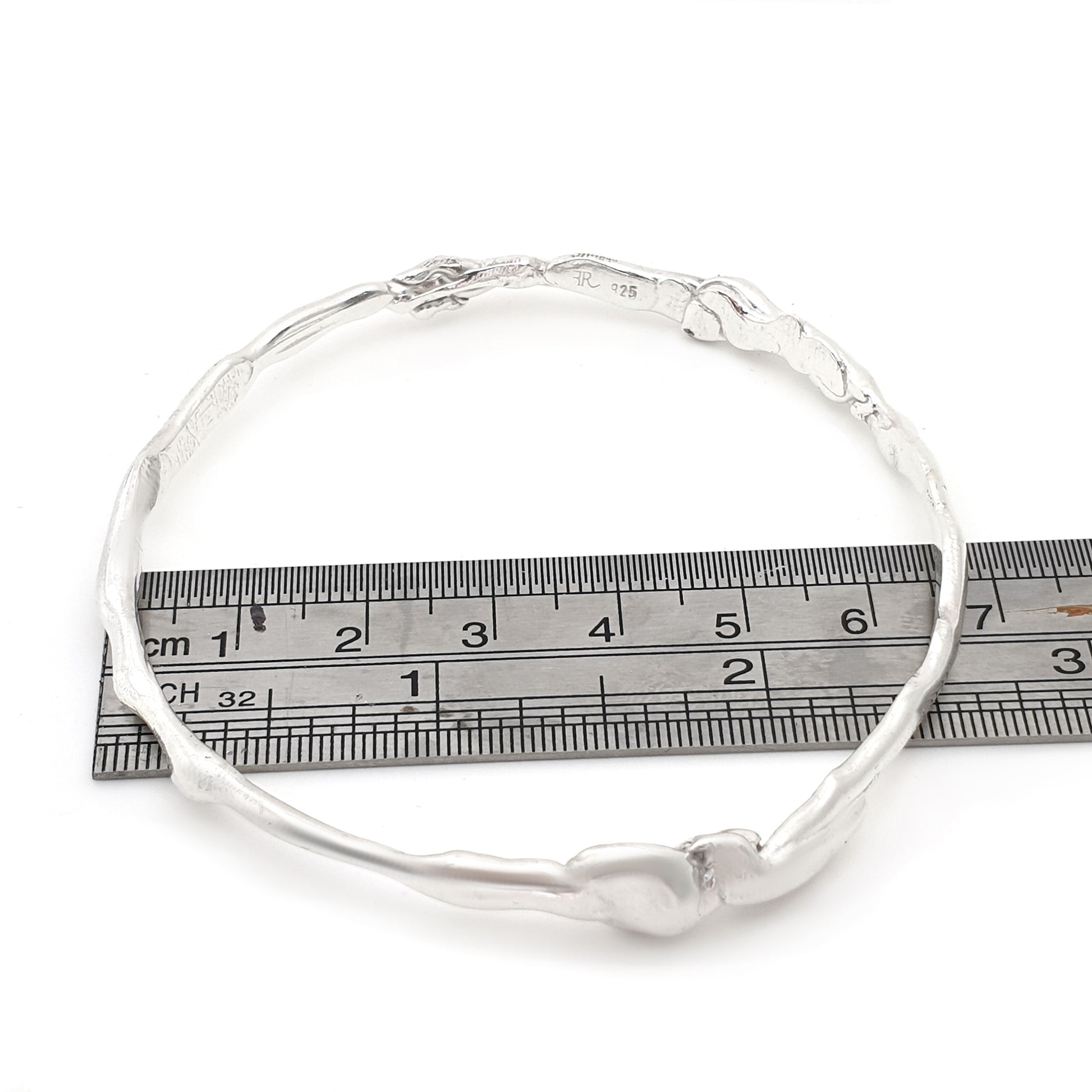 The Hoop Bangle by FR | Art Jewellery is shown with an organic, twisted design. Featuring an uneven, textured surface, it exudes a natural and unique charm. This piece of handmade jewellery is displayed against a white background and is available for custom-made orders.